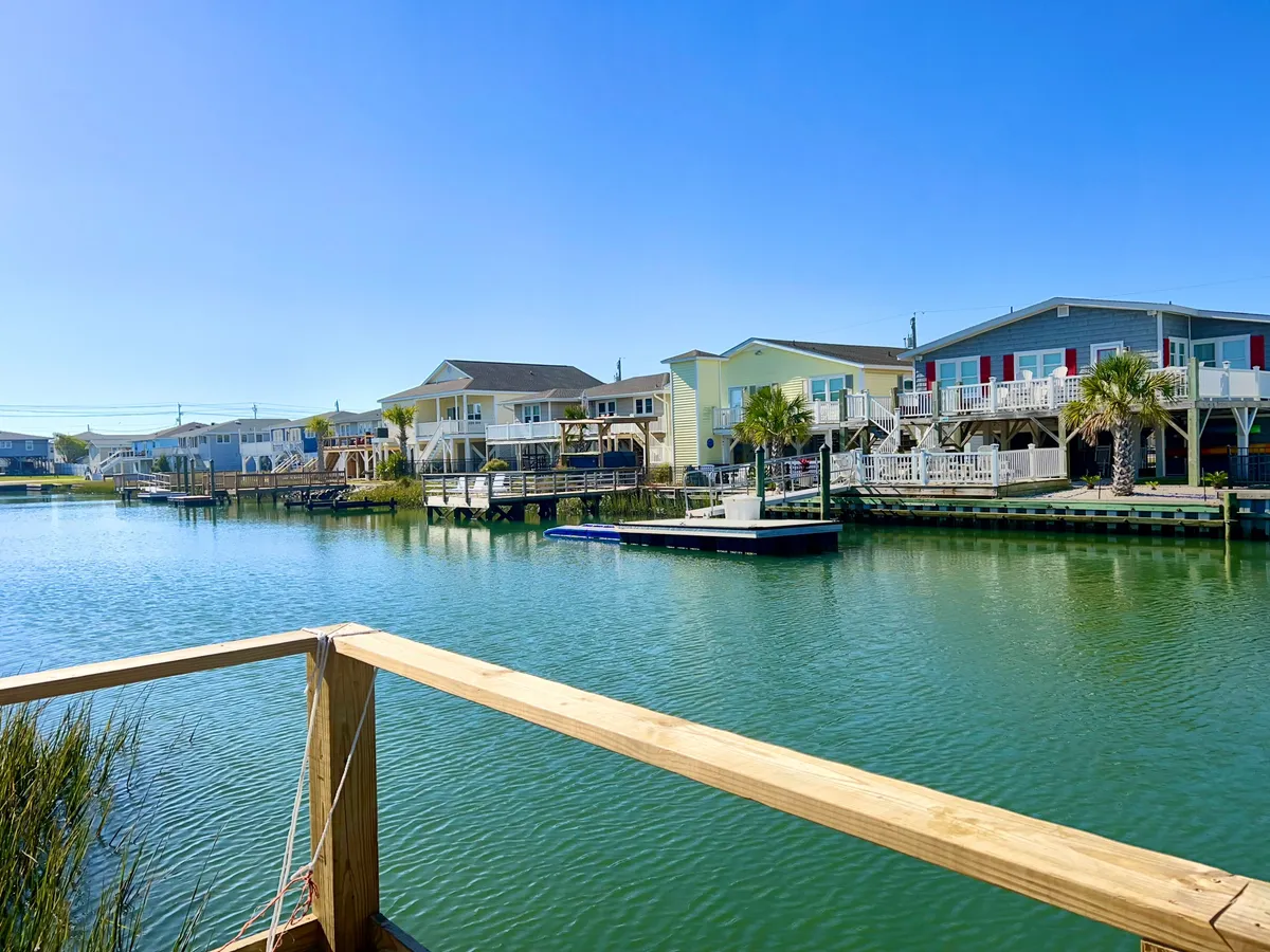 A wide view of houses lining a tranquil waterway, with a dock extending over clear blue water and palm trees adding to the relaxed setting. The scene invites leisurely walks along the waterfront and offers a sense of connection to outdoor activities.