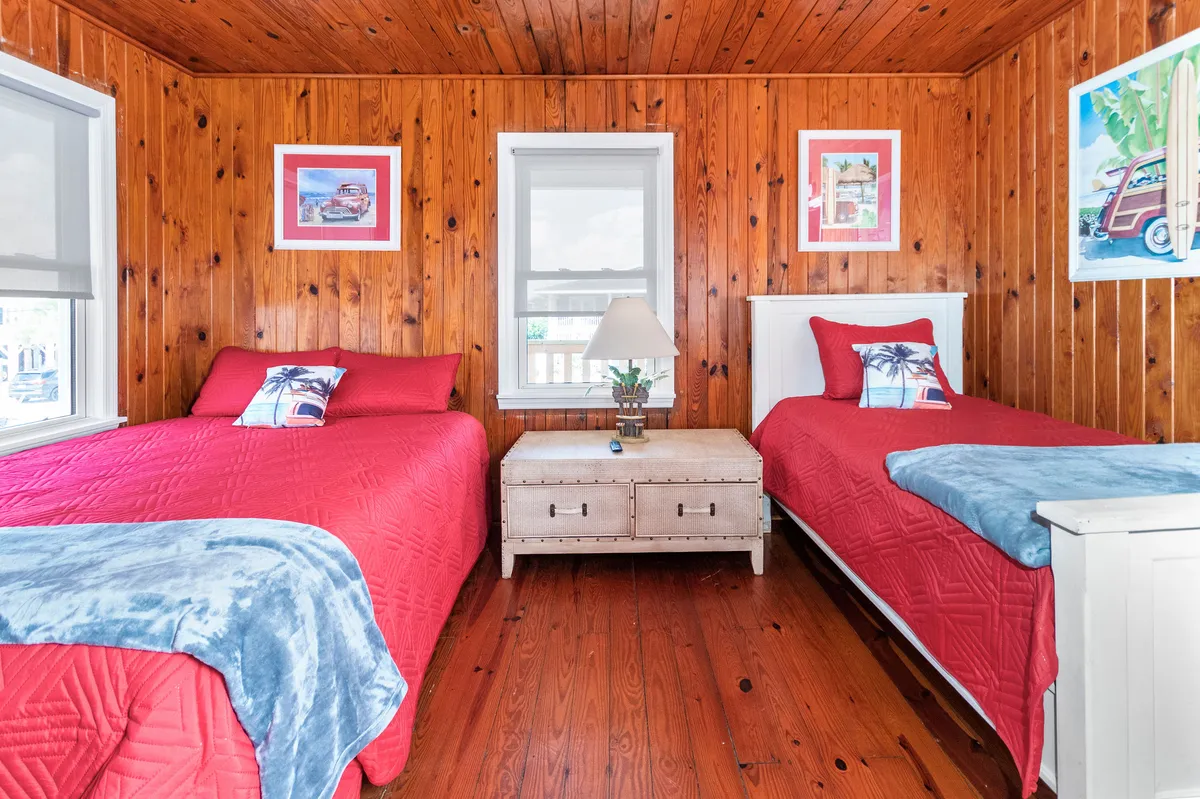 This interior image features two red beds set against wood-paneled walls, with decorative artwork and a nightstand with a lamp. The space feels bright and cheerful, ideal for restful nights or afternoon reading—a perfect example of an inviting upstairs bedroom.