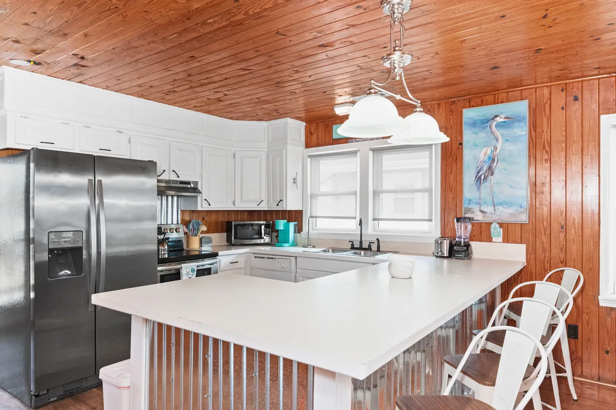 This image showcases an island kitchen counter with bar seating, a stainless steel refrigerator, and an eye-catching heron artwork. The layout is open and inviting, suggesting a space ideal for meal prep and socializing. The counters offer plenty of space for cooking, while the modern appliances hint at the kitchen's functionality.