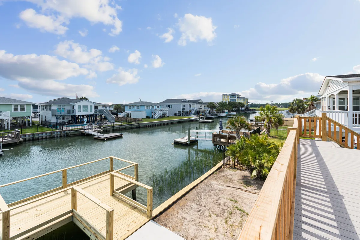 This image features a tranquil canal lined with palm trees, a boardwalk for easy shoreline access, and boats moored just steps away from the houses. The setting is vibrant yet peaceful, evoking the quintessential waterfront lifestyle and the proximity to water-based activities.