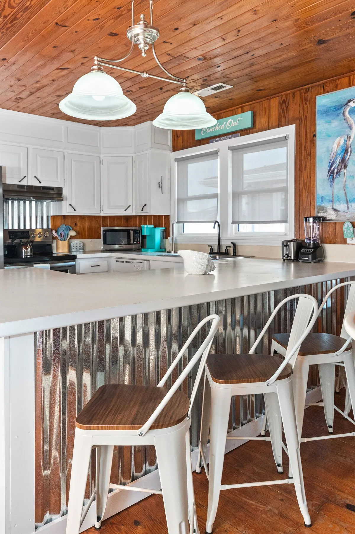 The kitchen features a central island, modern hanging light fixtures, contemporary appliances, and decorative wall art. The space feels bright and friendly, ideal for cooking or enjoying breakfasts together, and underscores the openness and functionality of the kitchen.