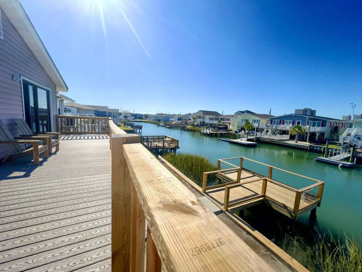 A serene view from the deck looking out over a wide waterway, with boat docks, houses, and calm waters visible. The tranquil setting offers an ideal spot for evening gatherings, quiet reflection, or launching into water-based adventures.