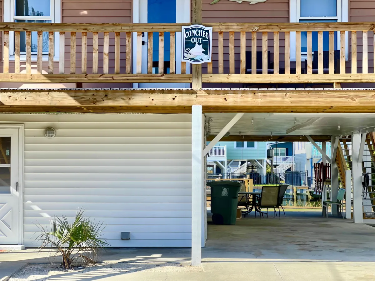 A welcoming exterior with a wooden railing, potted plant, and a 'CONCHED OUT' sign. The space suggests a shaded porch perfect for lounging and social gatherings after pet-friendly adventures.